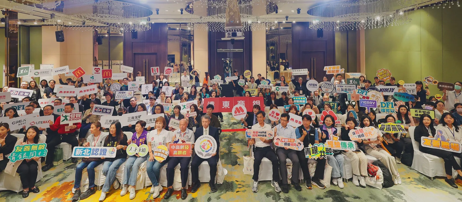 115 年度新北市中高齡者及高齡者友善職場認證表揚活動現場,獲證企業代表手持標語合影